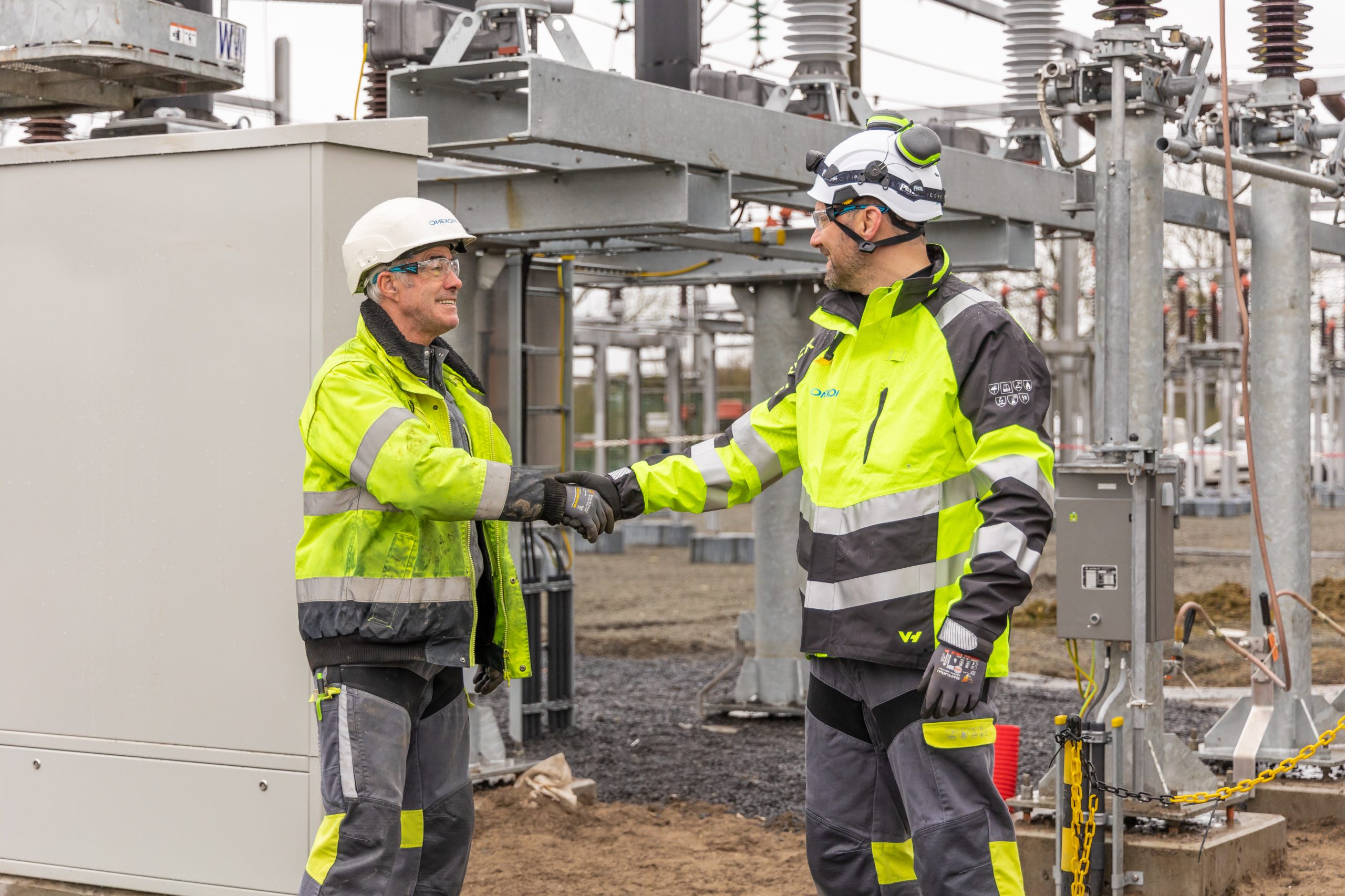 Two workers shaking hands in front of the substation