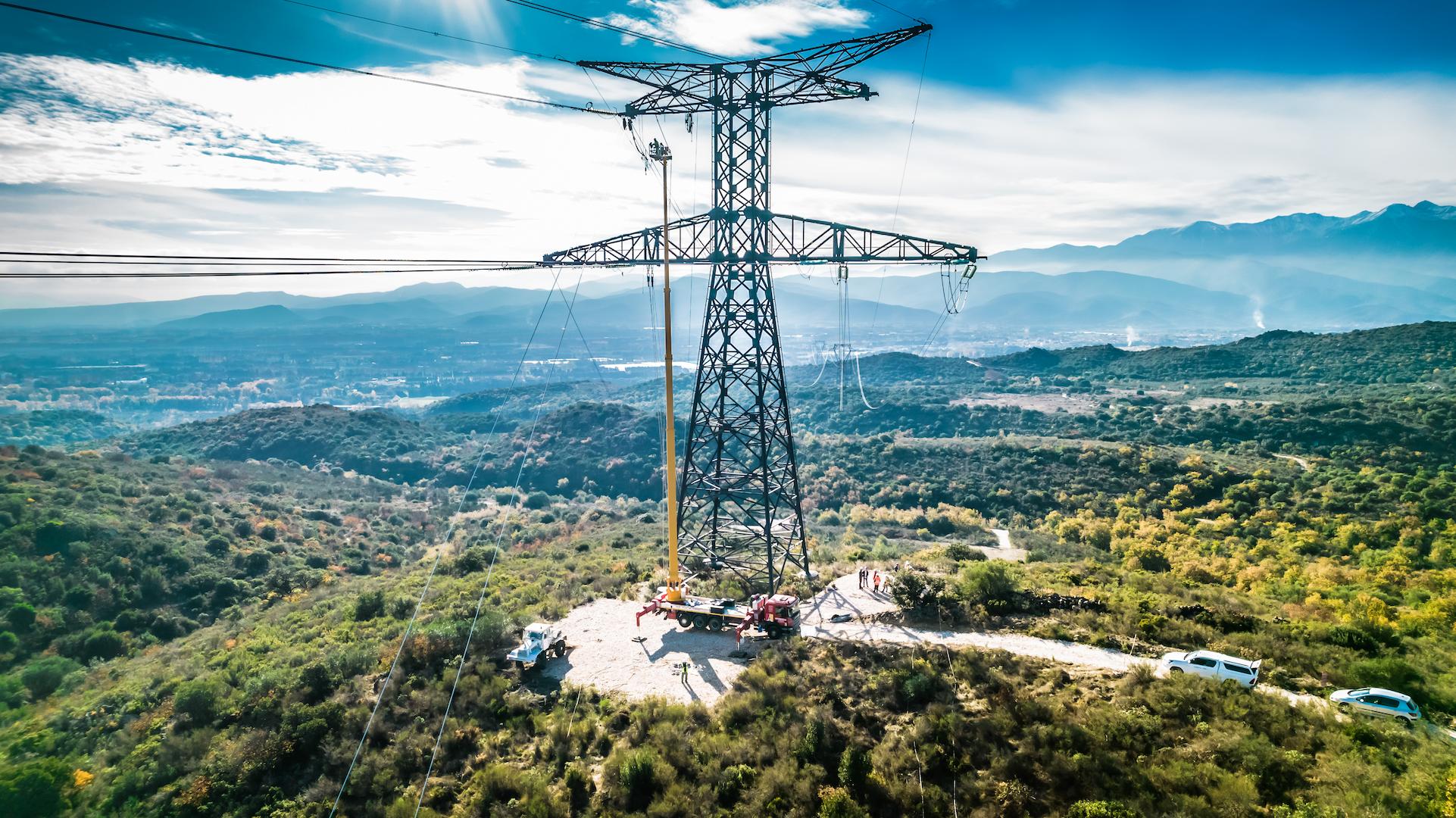 High-voltage transmission tower crossing a natural valley landscape, supporting long-distance power networks
