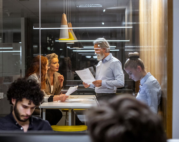Draufsicht auf vier Personen an einem Meetingtisch, die an Laptops, einem Tablet und einem Notizbuch arbeiten.
